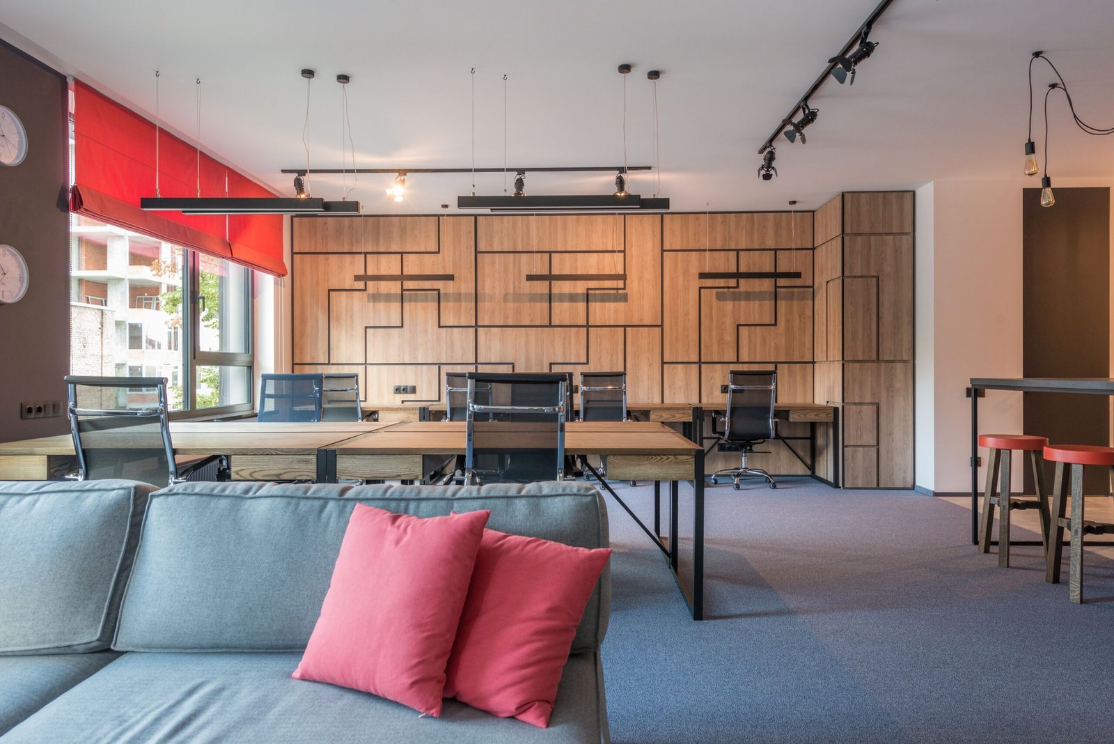 Home Sofa with cushions against tables and armchairs under hanging lamps in contemporary office in daylight